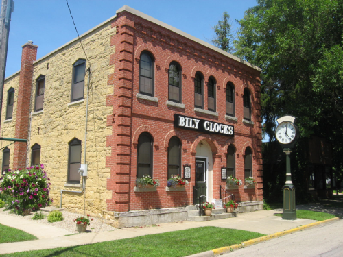Historic brick building with "Billy Clocks" sign, flower boxes, and a vintage clock on the sidewalk.