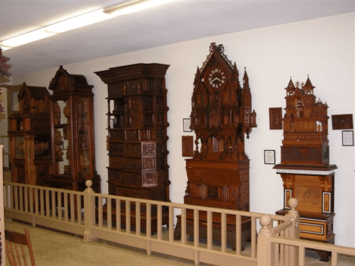 A display of intricately carved wooden clocks in a museum setting, showcasing various styles and designs.