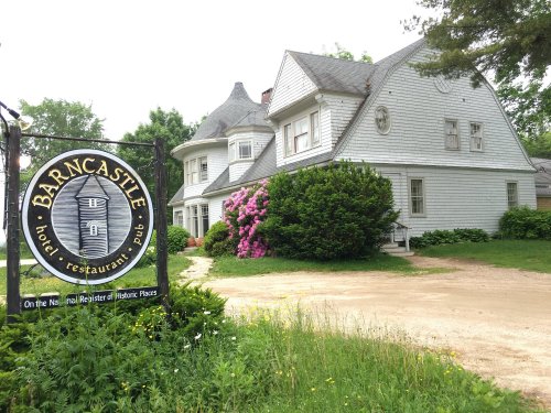 A historic building with a sign reading "Barncastle" for a hotel, restaurant, and pub, surrounded by greenery and flowers.
