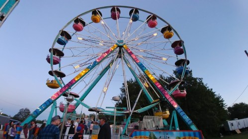 A colorful Ferris wheel at a fair, with people walking nearby and a twilight sky in the background.