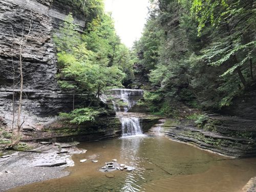 A serene waterfall cascades into a calm pool, surrounded by lush greenery and rocky cliffs.