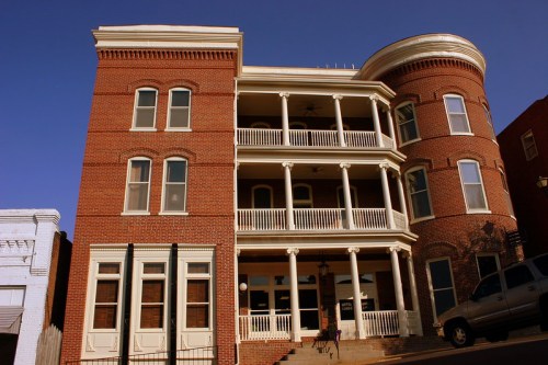 Historic brick building with multiple balconies and white railings, set against a clear blue sky.
