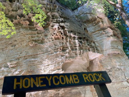 Sign reading "Honeycomb Rock" in front of a textured rock formation with greenery above.