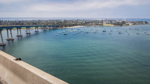 A scenic view of a bridge over water, with boats anchored in the bay and a shoreline in the background.