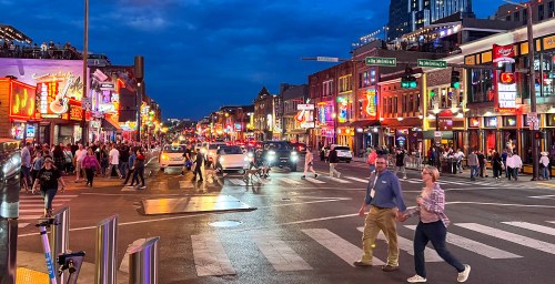 A bustling city street at night, filled with colorful lights, people walking, and cars navigating the busy scene.