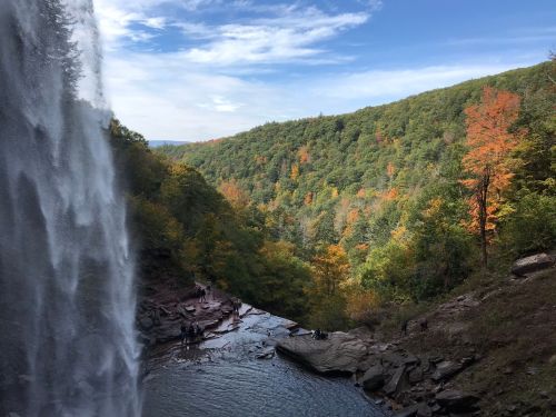 A scenic view of a waterfall cascading into a river, surrounded by colorful autumn foliage and hills.