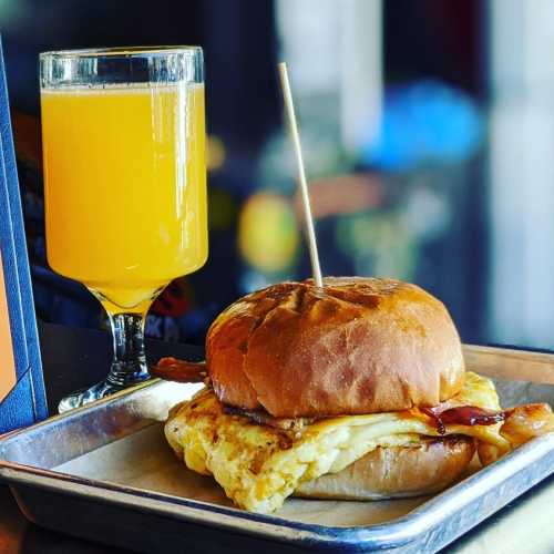 A golden sandwich with egg and bacon on a tray, accompanied by a glass of orange juice.