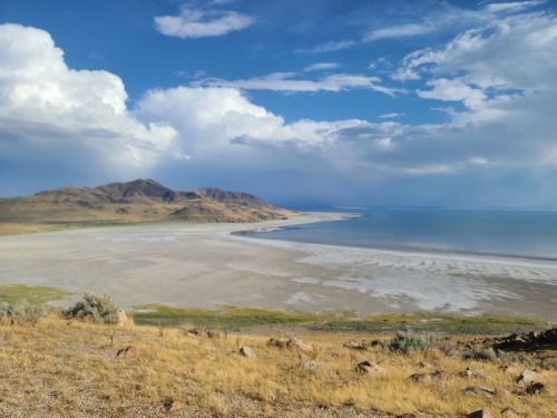 A scenic view of a vast, dry lakebed with mountains in the background under a cloudy sky.