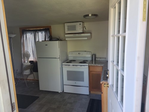 A view of a small kitchen with a refrigerator, stove, and microwave, seen from an open door.