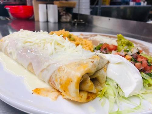 A plate of enchiladas topped with cheese, accompanied by rice, guacamole, pico de gallo, and shredded lettuce.