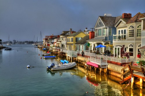 Colorful waterfront houses line a calm bay, with boats moored and a misty sky in the background.