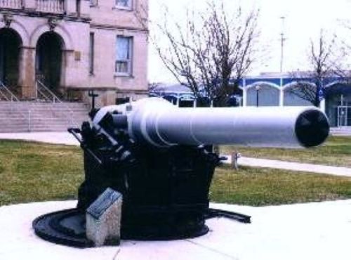 A large artillery cannon displayed outdoors, set on a grassy area near a building.
