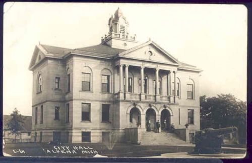 Historic city hall building with columns and a clock tower, surrounded by trees and a cannon in the foreground.