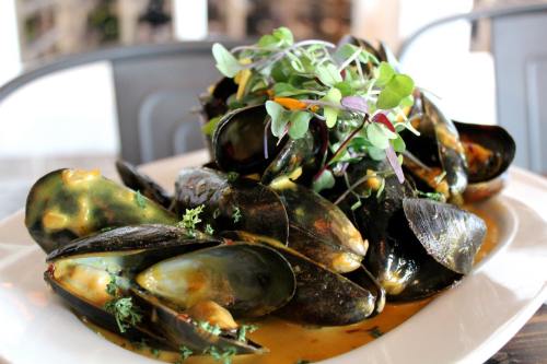 A plate of mussels in a flavorful sauce, garnished with fresh herbs and microgreens.
