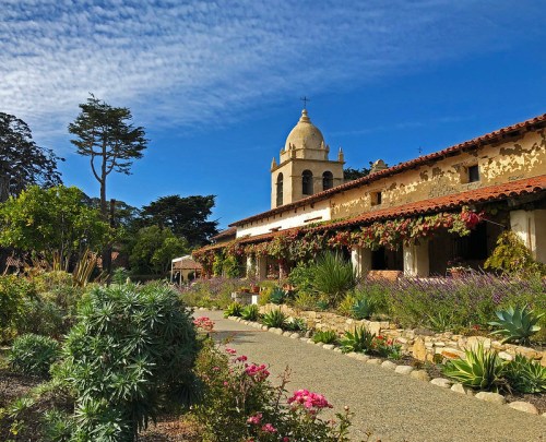 A scenic view of a historic building surrounded by lush gardens and blue skies.