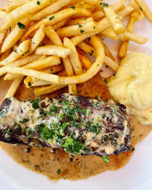 A plate featuring a grilled steak with creamy sauce, topped with herbs, served with golden fries and mashed potatoes.