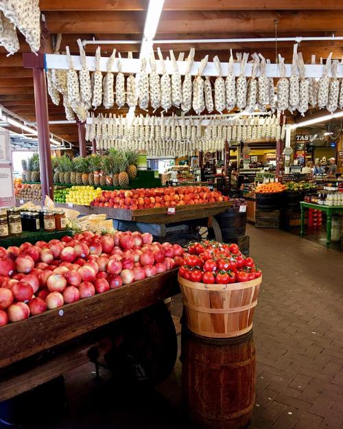 A vibrant market scene with colorful fruits, including apples and tomatoes, displayed on wooden carts and shelves.