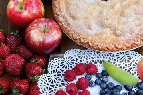 A rustic table with a pie, red apples, strawberries, and a plate of raspberries, blueberries, and green apple slices.