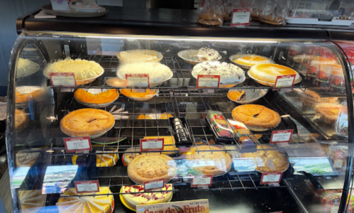 A display case filled with various pies and desserts, labeled with names and prices.