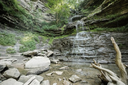 A serene waterfall cascading down rocky cliffs, surrounded by lush greenery and a calm pool of water below.