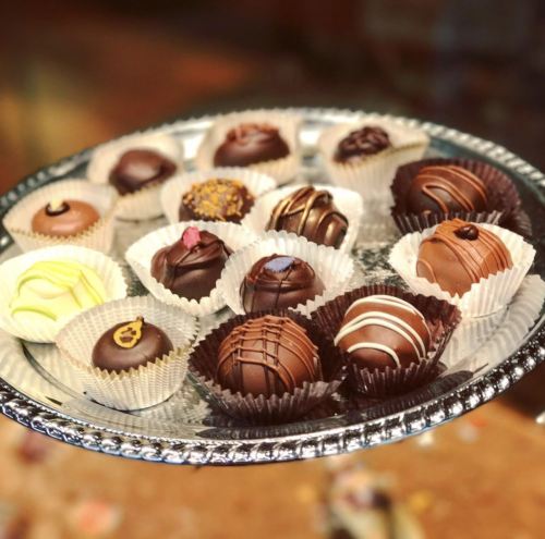 A silver tray filled with assorted chocolate truffles in paper cups, featuring various designs and toppings.