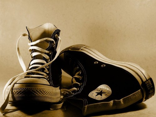 A pair of black Converse high-top sneakers with white laces, set against a soft, neutral background.