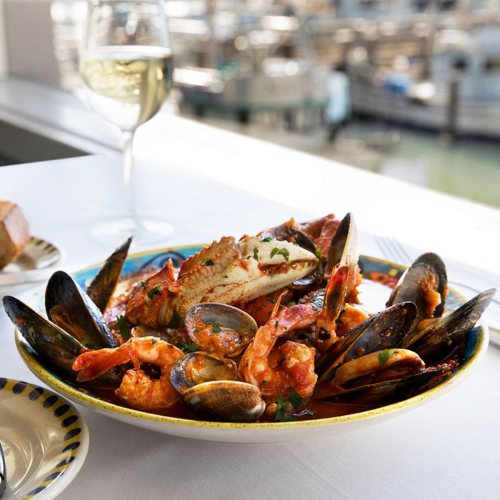 A colorful seafood dish with shrimp, mussels, and crab, served on a plate with a glass of white wine in the background.