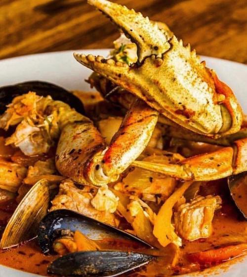 A close-up of a seafood dish featuring crab, mussels, and pieces of chicken in a rich, spicy sauce.