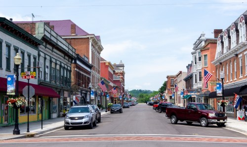 A charming small-town street lined with shops, flags, and parked cars under a clear blue sky.