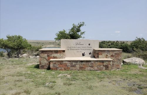 Welcome sign at Clayton Lake State Park, featuring dinosaur trackway information, surrounded by grassy landscape.