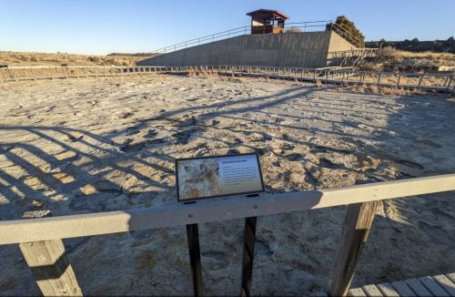 A barren landscape with a viewing platform and informational sign, showcasing a dry, cracked earth surface.