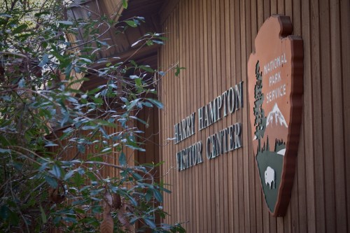Sign for the Harry Hampton Visitor Center, featuring the National Park Service logo, surrounded by greenery.
