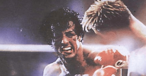A close-up of a boxer in a match, showing intense emotion and wearing red gloves.