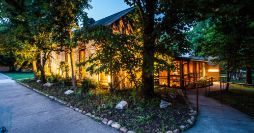 A charming brick building illuminated at dusk, surrounded by trees and a landscaped path.