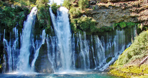 A scenic view of a waterfall cascading over rocky cliffs, surrounded by lush greenery and a clear blue pool below.