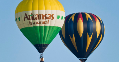 Two colorful hot air balloons in the sky, one green and yellow with "Arkansas" text, the other black and red.