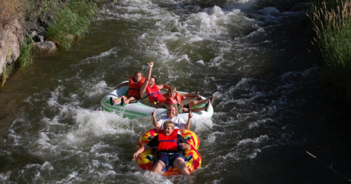 Four people enjoying a fun float down a river on inflatable tubes, surrounded by greenery and rushing water.