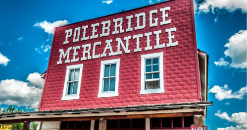 Red building with large white letters reading "Polebridge Mercantile" against a blue sky with fluffy clouds.