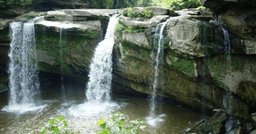 A serene waterfall cascading over rocky cliffs into a calm pool, surrounded by lush greenery.