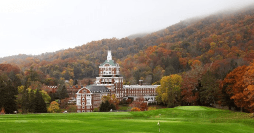 A grand hotel surrounded by colorful autumn trees and rolling hills, with a misty mountain backdrop.