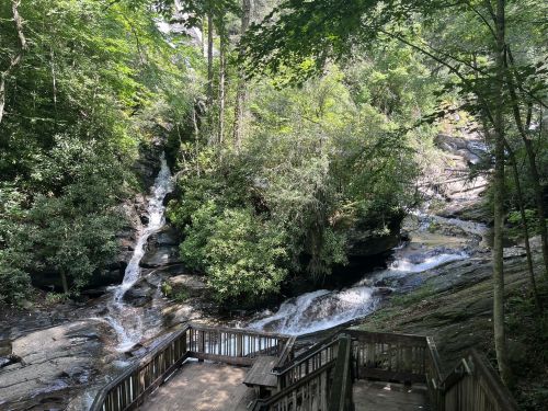 A serene view of cascading waterfalls surrounded by lush greenery and rocky terrain, with a wooden viewing platform.