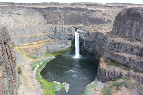 A waterfall cascades into a circular pool, surrounded by rocky cliffs and sparse vegetation.