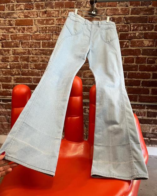 Light blue flared jeans displayed on a red chair against a brick wall background.