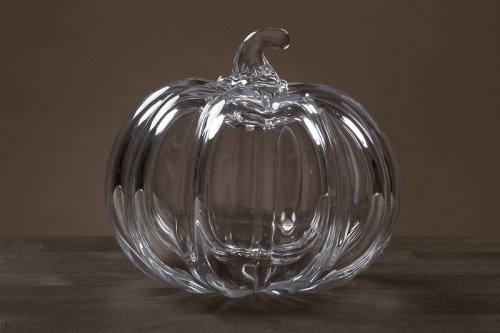 A clear glass pumpkin sculpture with a curved stem, sitting on a wooden surface against a neutral background.