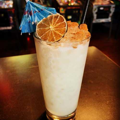 A refreshing cocktail in a tall glass, garnished with a dried lime slice and a blue paper umbrella.