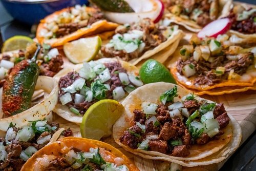 A colorful assortment of tacos topped with onions, cilantro, and lime, served on a wooden platter.