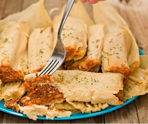 A plate of tamales with a fork piercing one, showcasing the filling and garnished with herbs.