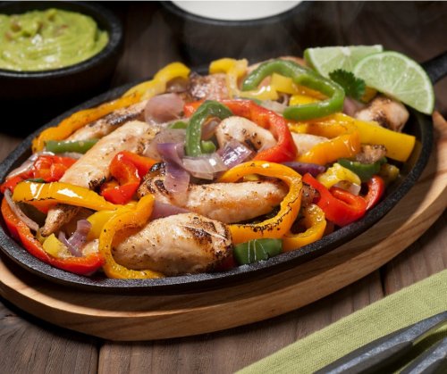 Sizzling fajitas with grilled chicken, colorful bell peppers, and onions on a hot skillet, served with lime and guacamole.