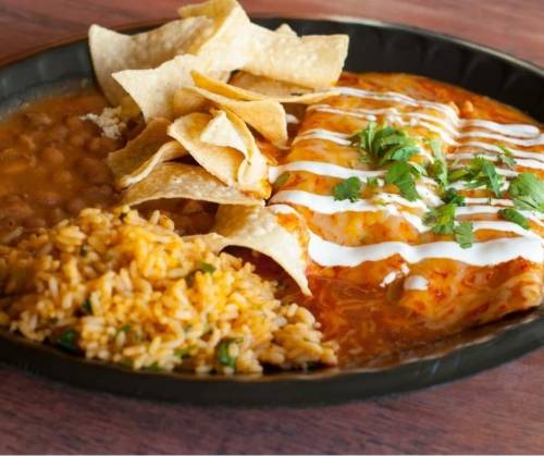 A plate of enchiladas topped with sour cream and cilantro, served with rice, beans, and tortilla chips.