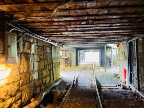 View of a dimly lit tunnel with stone walls and railway tracks leading to an open area ahead.